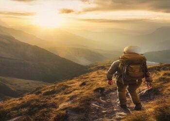 Adventure traveller hiking on a mountain trail at sunrise with a backpack