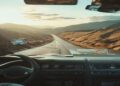 Open road through scenic hills seen from a car with a travel map and coffee on the dashboard
