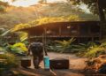 Traveler arriving at a small eco lodge surrounded by greenery with a suitcase and reusable water bottle