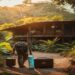 Traveler arriving at a small eco lodge surrounded by greenery with a suitcase and reusable water bottle